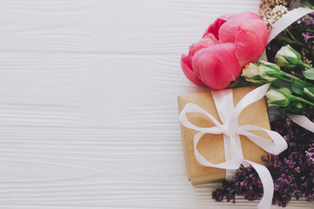 Stylish simple gift box and bouquet flat lay with peony, lilac and roses flowers on white wooden...