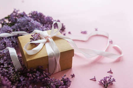 Lilac flowers, gift box and heart ribbon on pink paper. Stylish floral greeting card. Happy valentines day and mothers day concept. Purple lilac bouquet with stylish craft presentの写真素材