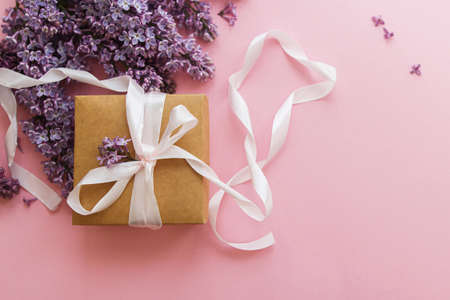 Lilac flowers and gift box on pink paper, stylish flat lay. Happy mothers day and womens day concept. Spring floral greeting card. Purple lilac bouquet with craft present and ribbonの写真素材