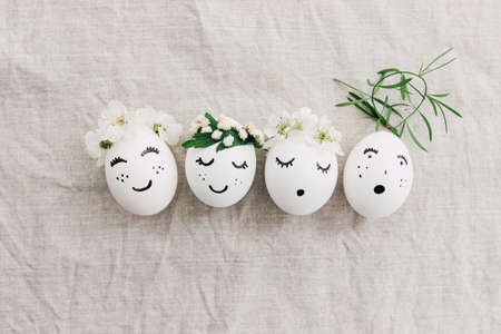 Natural eggs with drawn funny faces in cute floral crowns top view on linen fabric with blooming...