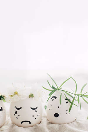 Natural easter eggs with drawn sad crying faces in floral wreaths on linen fabric in soft light....