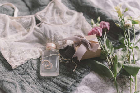 Happy Women's day. Stylish gift box, modern jewelry, perfume bottle and lace lingerie on cozy green sweater with spring flowers on bed. Soft tender and trendy feminine image. Woman essentialsの写真素材