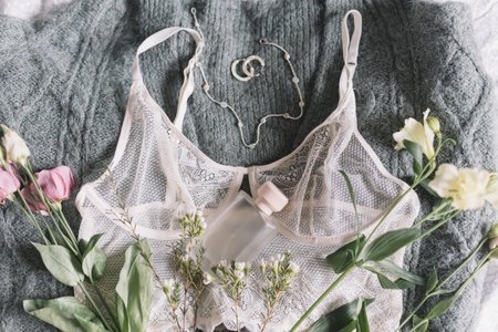 Happy Women's day. Stylish perfume bottle, modern jewelry and lace lingerie with spring flowers on cozy green sweater on bed. Soft tender and trendy feminine image. Woman essentials, fragranceの写真素材