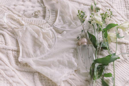 Happy Women's day. Stylish lace lingerie, perfume bottle, modern jewelry and spring flowers on cozy beige sweater. Soft trendy feminine image. Woman essentials, fragranceの写真素材