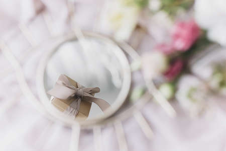 Stylish gift box reflected in mirror on background of soft fabric with flowers. Happy Womens and Mothers day. Giving present concept, gentle image. Eye shape boho mirror and bouquetの写真素材