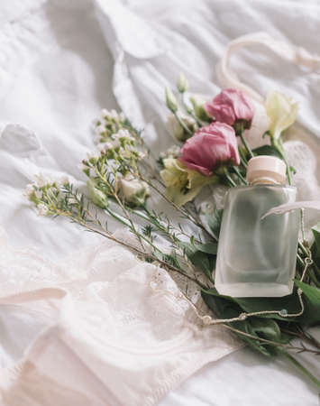 Happy Women's day. Stylish lace lingerie, modern jewelry, perfume bottle and spring flowers on shirt on bed. Soft trendy feminine image, sensual mood at home concept. Woman essentials, fragranceの写真素材