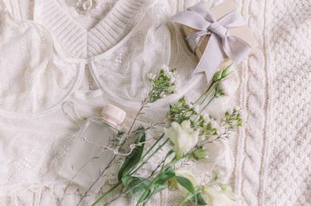 Happy Women's day. Stylish lace lingerie, perfume bottle, modern jewelry and gift box on cozy beige sweater with spring flowers. Soft trendy feminine image. Woman essentials, fragranceの写真素材