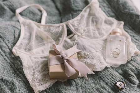 Stylish gift box, modern jewelry, perfume bottle and lace lingerie on cozy green sweater on bed. Soft tender and trendy feminine image. Happy Women's day, woman essentialsの写真素材