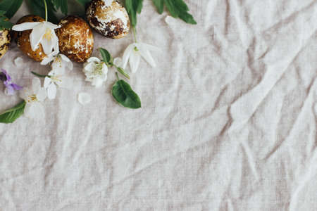 Easter eggs with spring flowers on rustic linen background, flat lay, space for text. Aesthetic seasons greetings. Stylish modern easter quail eggs in natural dye and spring bloomsの写真素材