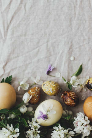 Easter rustic flat lay. Easter eggs with spring flowers on linen background with space for text. Aesthetic stylish easter eggs in natural dye and tender spring blooms and petalsの写真素材
