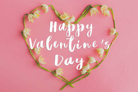 Happy Valentine's day text on floral heart made of spring flowers on pink paper flat lay. Love concept. Valentines day stylish greeting cardの写真素材