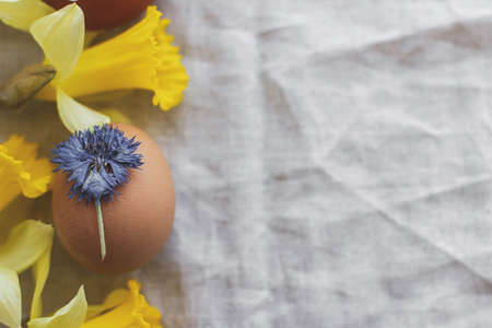 Happy Easter! Stylish Easter egg decorated with dry blue flower  on rustic linen napkin with yellow...