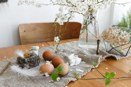 Natural Easter eggs, white bunnies, feathers, nest and cherry blooming branch with petals on rustic...