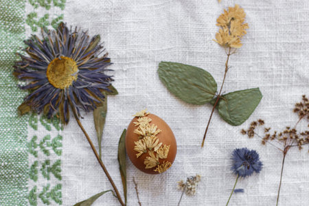 Easter egg decorated with dry flower on background of linen napkin and wildflowers. Top view....