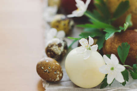 Stylish easter eggs and blooming spring flowers close up on linen napkin on rustic table. Happy...