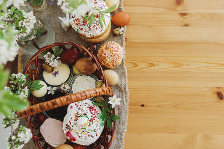 Delicious Easter food, stylish easter eggs, beets, cheese, butter, ham, homemade Easter bread in wicker basket with blooming spring flowers on rustic table, top view. Happy Easter! Orthodoxの写真素材