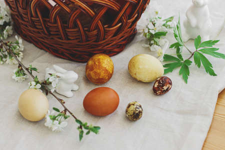 Stylish easter eggs, wicker basket, bunny figurine and spring blooming flowers anemones on rustic...