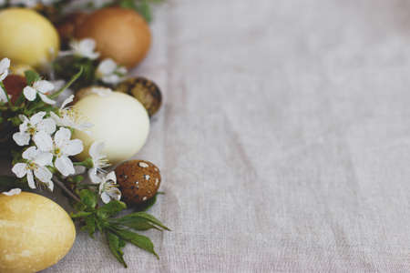 Modern pastel easter eggs with spring flowers on rustic linen cloth background, space for text. Happy Easter! Natural dyed egg in yellow and brown on grey textile with blooming flowers. Aestheticの写真素材