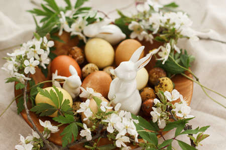 Modern easter eggs with spring flowers and bunny in wooden bowl on rustic linen cloth. Happy Easter!...