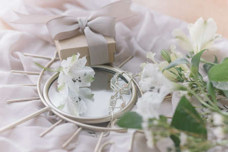 Happy Womens and Mothers day. Stylish gift box, modern jewelry and spring flowers on boho mirror on soft fabric. Gentle feminine image. Eye shaped mirror with manuka, alstroemeria flower and presentの写真素材