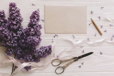 Beautiful lilac flowers, greeting card and vintage scissors on white rustic wooden background, flat...