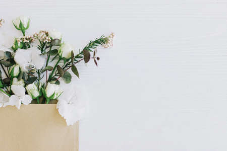 Stylish roses, hydrangea, and eucalyptus branches growing from craft envelope on white wood, flat lay with copy space. Floral Greeting card and flower delivery. Hello spring. Happy womens dayの写真素材