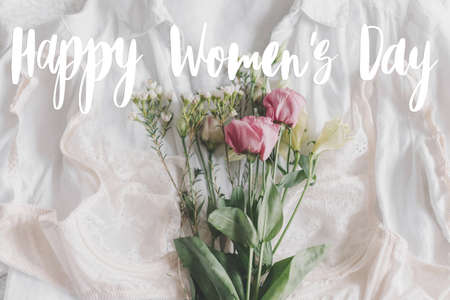 Happy womens day text on stylish lace lingerie, spring flowers on bed. Modern greeting card. Stylish...