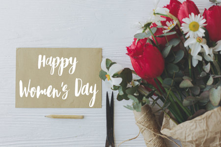 Happy womens day text on card and tulips, daffodils bouquet, pencil, scissors and twine on rustic white wood. Modern greeting card. Stylish handwritten sign. International women's dayの写真素材