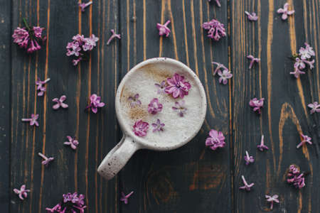 Coffee with lilac petals flat lay on dark wooden background with space for text. Fresh aromatic coffee in stylish cup and purple petals on rustic wood. Morning rituals aestheticの写真素材