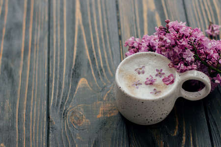 Coffee with lilac petals and blooming branch on dark wooden background with space for text. Fresh...