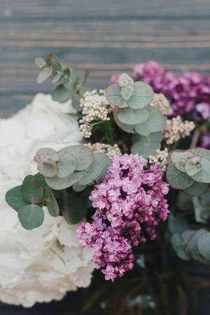 Beautiful lilac, eucalyptus and white hydrangea flowers on dark wooden background. Spring stylish fresh bouquet composition on rustic wood, floral still lifeの写真素材