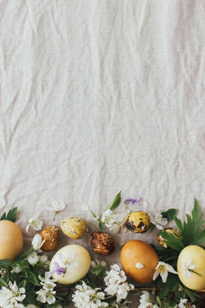 Easter eggs with spring flowers on rustic linen background, flat lay with space for text. Stylish...