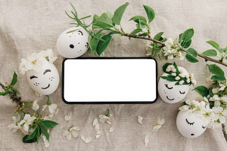 Phone with blank empty screen on background of easter eggs with drawn cute faces in floral wreaths...