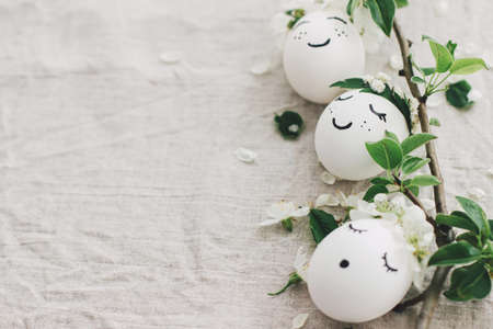 Natural eggs with drawn funny faces in cute floral wreaths on linen fabric with blooming spring...