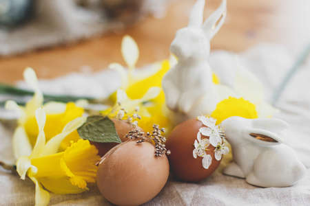 Stylish Easter eggs decorated with dry flowers and petals on rustic linen napkin with yellow daffodils and white bunnies. Happy Easter greeting card. Space for text. Creative eco friendly decorの写真素材