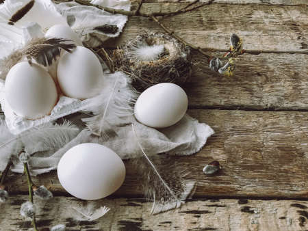 Natural easter eggs, feathers, pussy willow branches, bird nest on rustic cloth on aged wooden table. Stylish Rural still life. Simple easter aesthetics, brown and grey colorsの写真素材