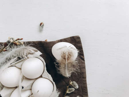 Natural easter eggs, feathers, pussy willow branches on rustic cloth on white aged table, flat lay. Modern simple aesthetics, white and grey colors. Stylish rural Easter still life. Space for textの写真素材
