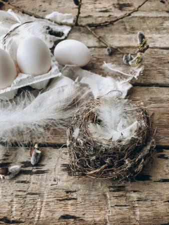 Simple stylish Easter still life. Bird nest, natural easter eggs, feathers, pussy willow branches on rustic cloth on aged wooden table. Rural natural easter aesthetic, brown and grey colorsの写真素材