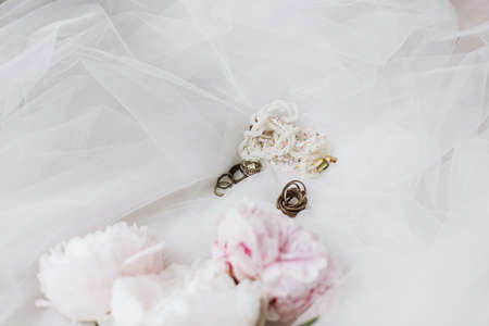 Stylish vintage accessories on soft tulle fabric with peony bouquet. Beautiful modern jewelry and pink and white peony flowers. Bridal morning. Feminine essentialsの写真素材