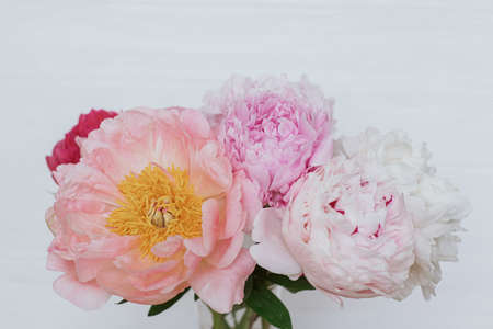 Beautiful peony bouquet in glass vase on white wooden background, copy space. Happy Mothers day. Womens day. Big pink and white peonies flowers in roomの写真素材
