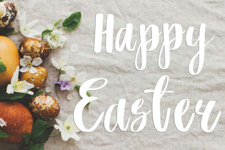 Happy Easter greeting card. Happy Easter text sign handwritten on  modern yellow easter eggs with spring flowers and blossoms on rustic fabric. Beautiful postcard, seasons greetingsの写真素材