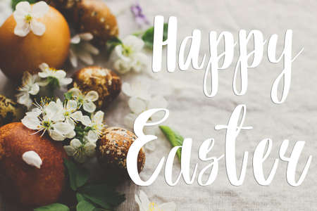 Happy Easter greeting card. Happy Easter text sign handwritten on  modern yellow easter eggs with spring flowers and blossoms on rustic fabric. Beautiful postcard, seasons greetingsの写真素材
