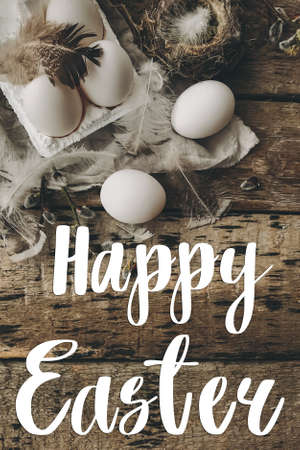 Happy Easter text on easter eggs, feathers, pussy willow branches, bird nest on rustic cloth on aged wood, handwritten sign. Beautiful stylish greeting card. Seasons greetingsの写真素材