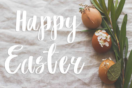 Happy Easter greeting card. Happy Easter text sign handwritten on  Easter eggs decorated with flowers on rustic linen napkin with green branch. Beautiful postcard, seasons greetingsの写真素材