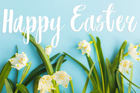 Happy Easter text on white spring snowflakes flowers growing on blue background, handwritten sign. Beautiful stylish greeting card. Seasons greetingsの写真素材
