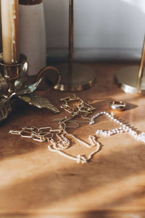 Modern gold and pearl accessories on table with vintage candlesticks. Stylish golden necklace and...