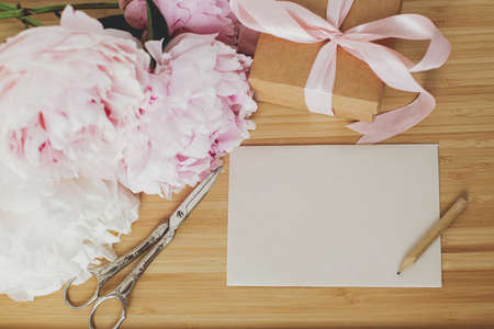 Beautiful peony bouquet, stylish gift box, greeting card and scissors on wooden background, top view with copy space. Happy Mothers day. Pink and white peonies and presentの写真素材