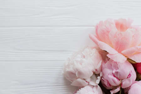 Beautiful tender peony flowers border on white wood with copy space. Happy Mothers day. Lovely pink and white peonies bouquet on rustic white wood. Floral greeting cardの写真素材