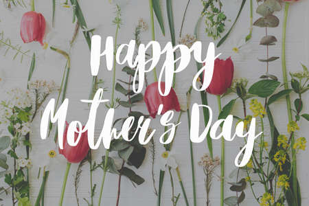 Happy mother's day. Happy mother's day text and red tulips, daffodils flowers and wildflowers composition on white wood flat lay. Stylish floral greeting card. Handwritten lettering. Mothers dayの写真素材