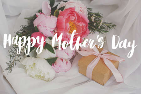 Happy mother's day greeting card. Happy mother's day text and  beautiful peonies bouquet, gift box on soft white fabric. Stylish floral greetings. Handwritten lettering. Mothers dayの写真素材
